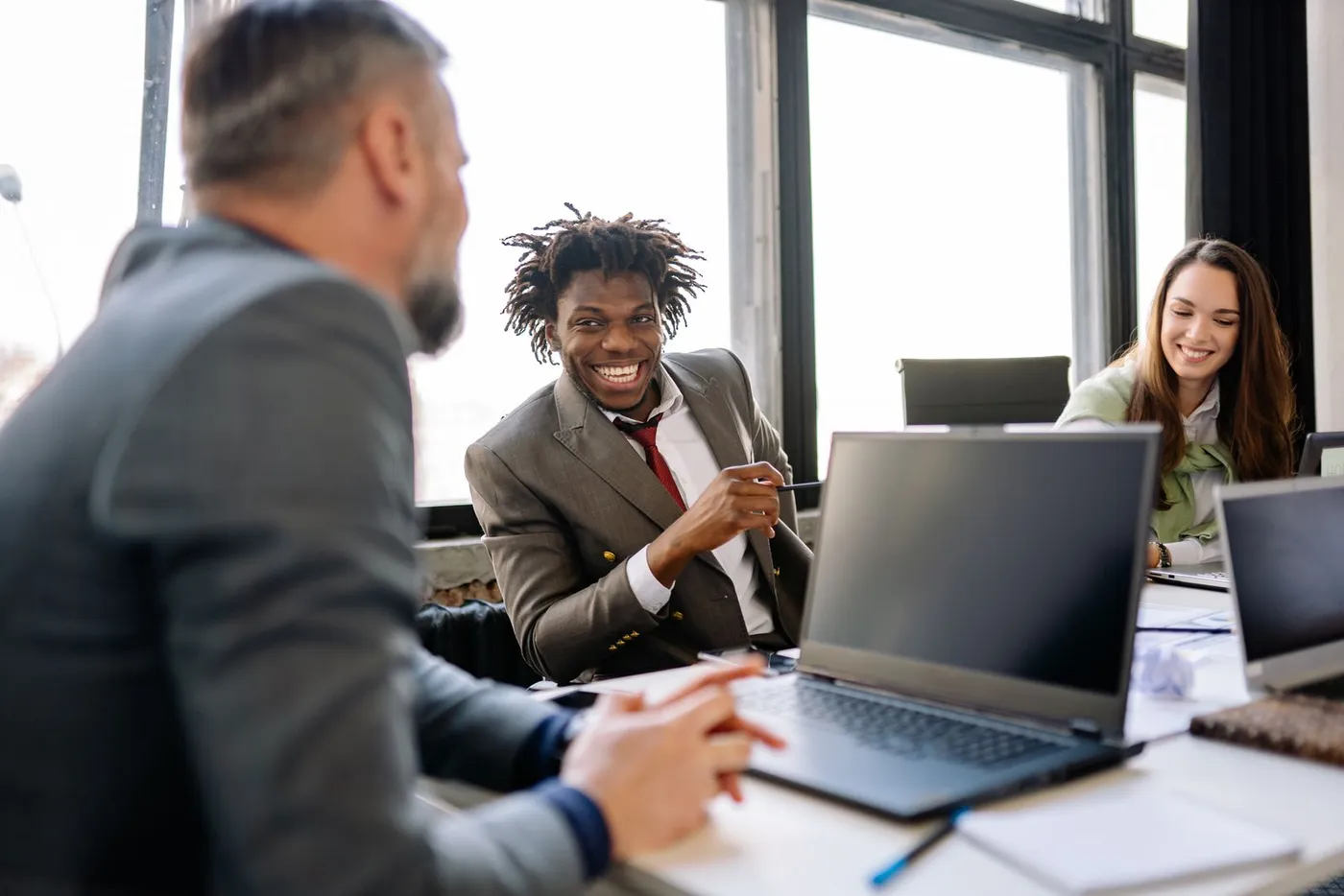 Trois collègues rient ensemble devant des ordinateurs portables dans un bureau lumineux